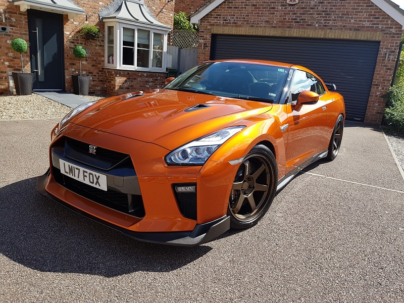 a super glossy orange Nissan GTR parked in the sun.